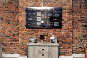 A wall-mounted digital display with a welcome message, QR codes, and a view of Liverpool.