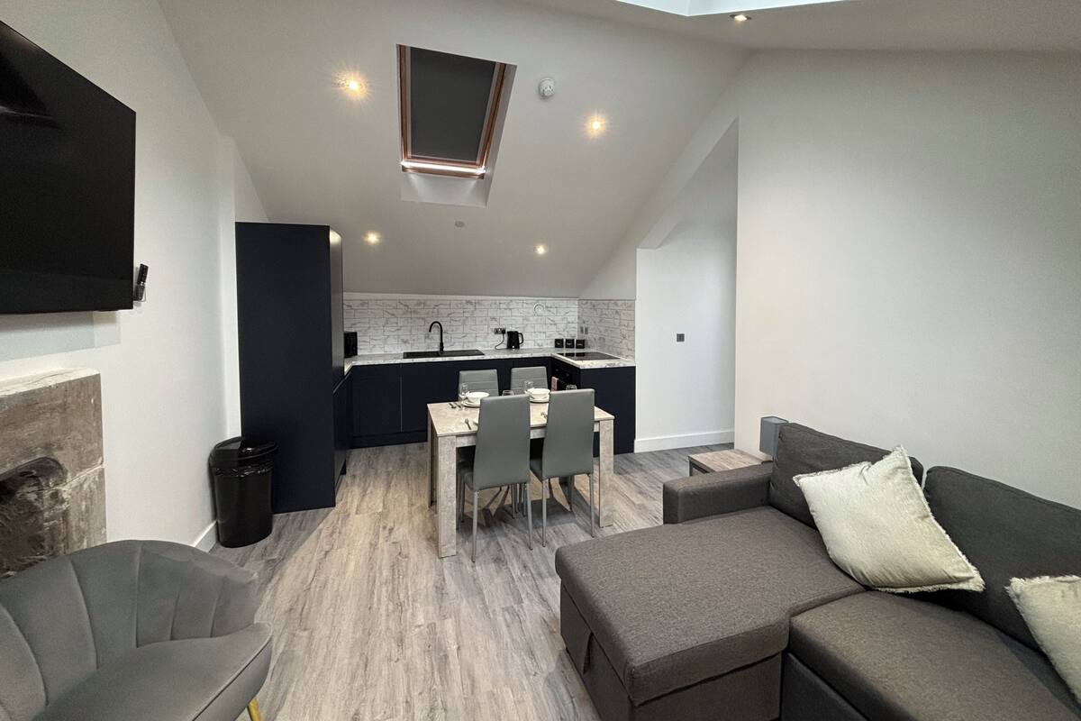 A modern kitchen with a skylight, a dining area with a table and chairs, and a grey sofa with a cushion.