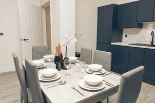 Un comedor moderno con una mesa dispuesta para seis personas, copas y botellas de vino, en una habitación con armarios oscuros y suelo de color claro.