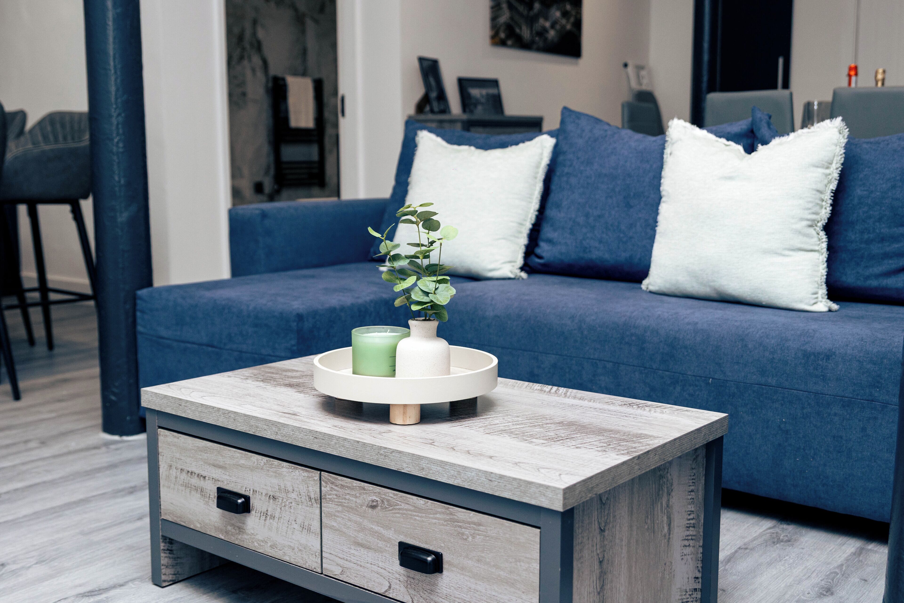 A modern living room with a blue sofa, white pillows, a coffee table with a plant, and a side table with drawers.