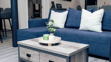 A modern living room with a blue sofa, white pillows, a coffee table with a plant, and a side table with drawers.