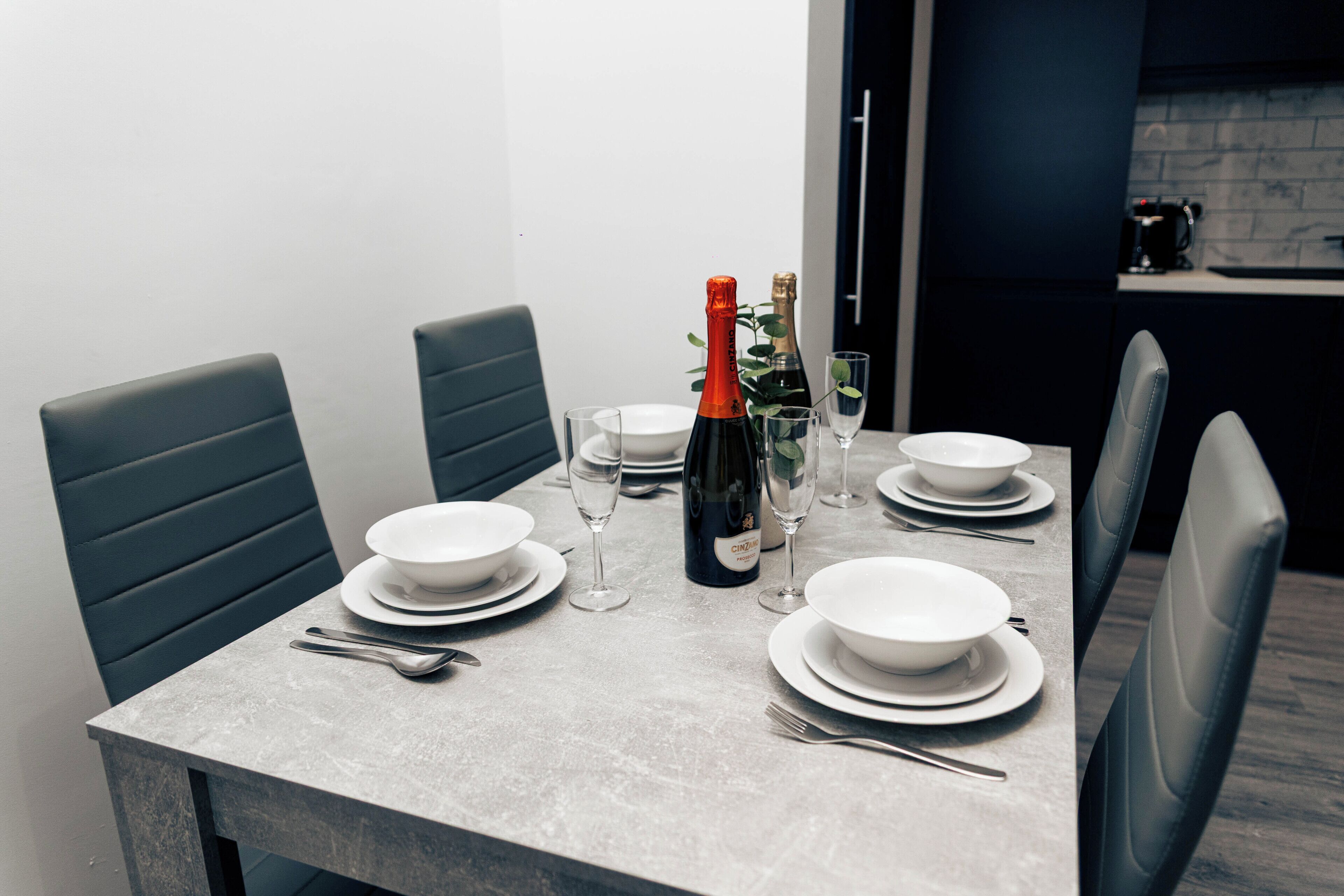 Une table à manger dressée avec des assiettes, des verres et une bouteille de vin, entourée de chaises.