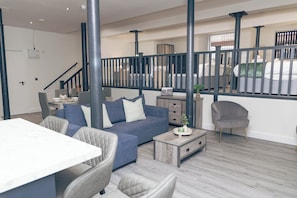 A modern living room with a sofa, chairs, a coffee table, and a staircase with a railing. - Cumberland Street Apartments (Liverpool)