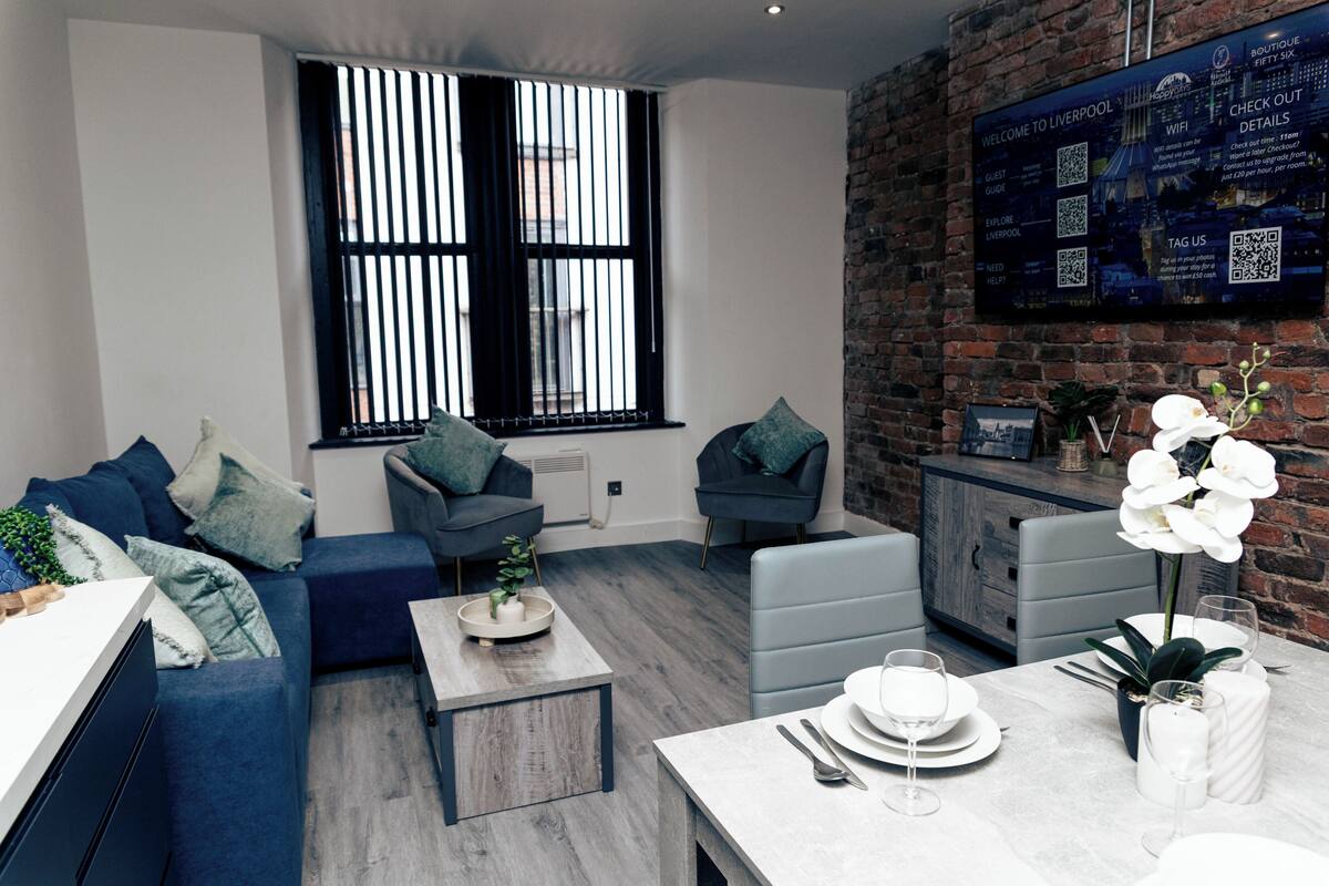 A modern living room with a sofa, armchairs, a coffee table, and a dining area with a table set for two.