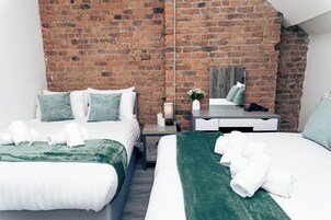 Habitación de hotel con dos camas, una pared de ladrillo, un espejo, un escritorio y una mesita de noche.