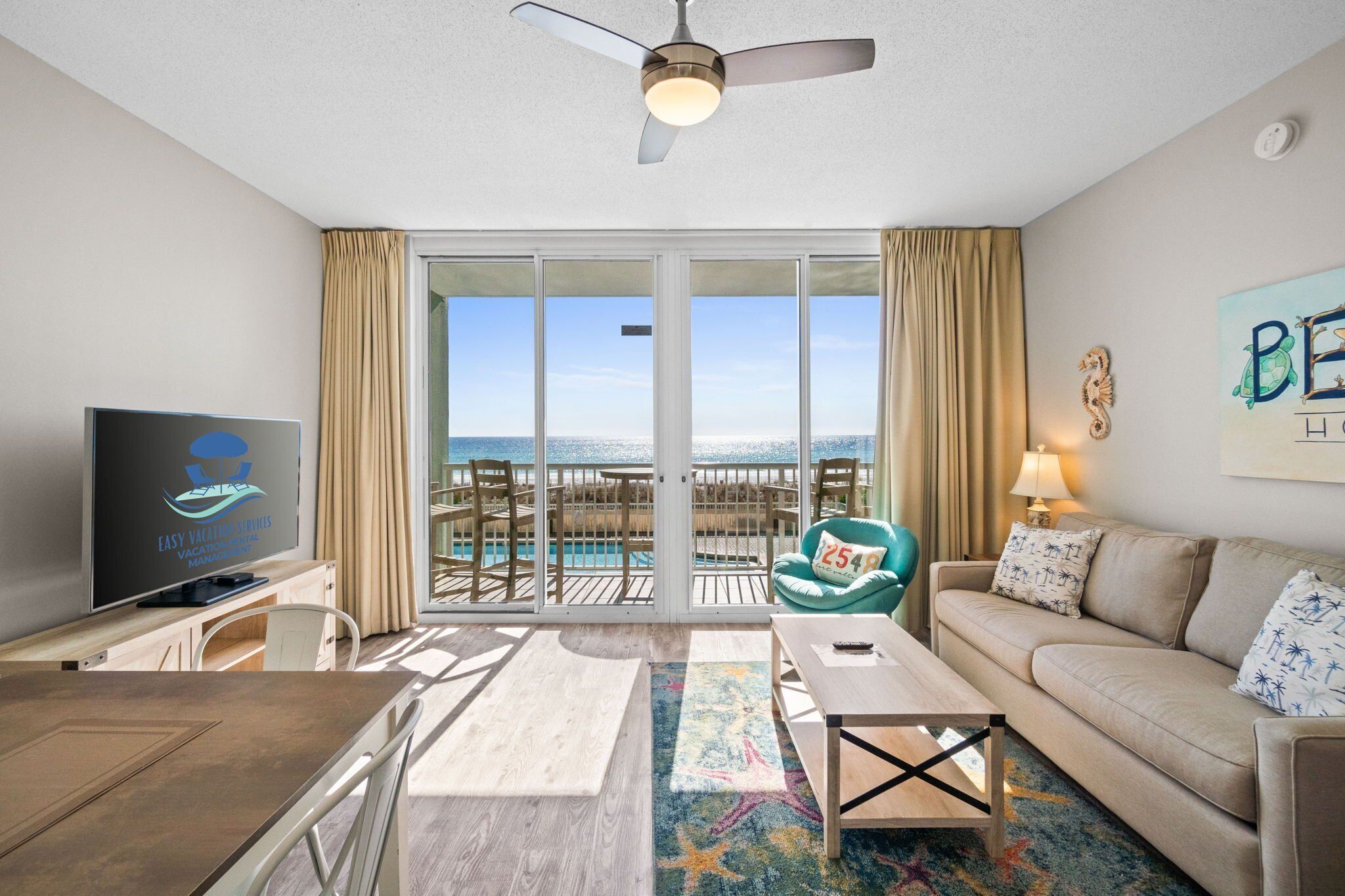 A hotel room with a balcony, a television, a sofa, a coffee table, and a view of the ocean.