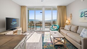 Une chambre d’hôtel avec un balcon, une télévision, un canapé, une table basse et une vue sur l’océan.