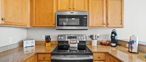 A kitchen with wooden cabinets, a stainless steel microwave, a stove, and a coffee maker.