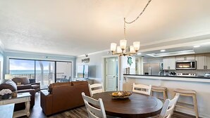 Una cocina moderna con armarios blancos, una isla central y un comedor con una mesa redonda y sillas blancas.