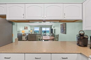 A kitchen with white cabinets, a granite countertop, and a view of the ocean through a window. - Island Echos 4P-Reef Intermission Beachfront Bliss in Fort Walton Beach, Perfect for Family Getaways (Fort Walton Beach)