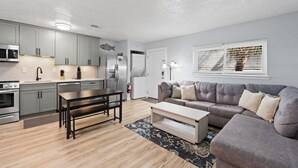 Eine moderne Küche mit grauen Schränken, einem Esstisch und einem grauen Sofa in einem Wohnbereich mit einem Fenster.