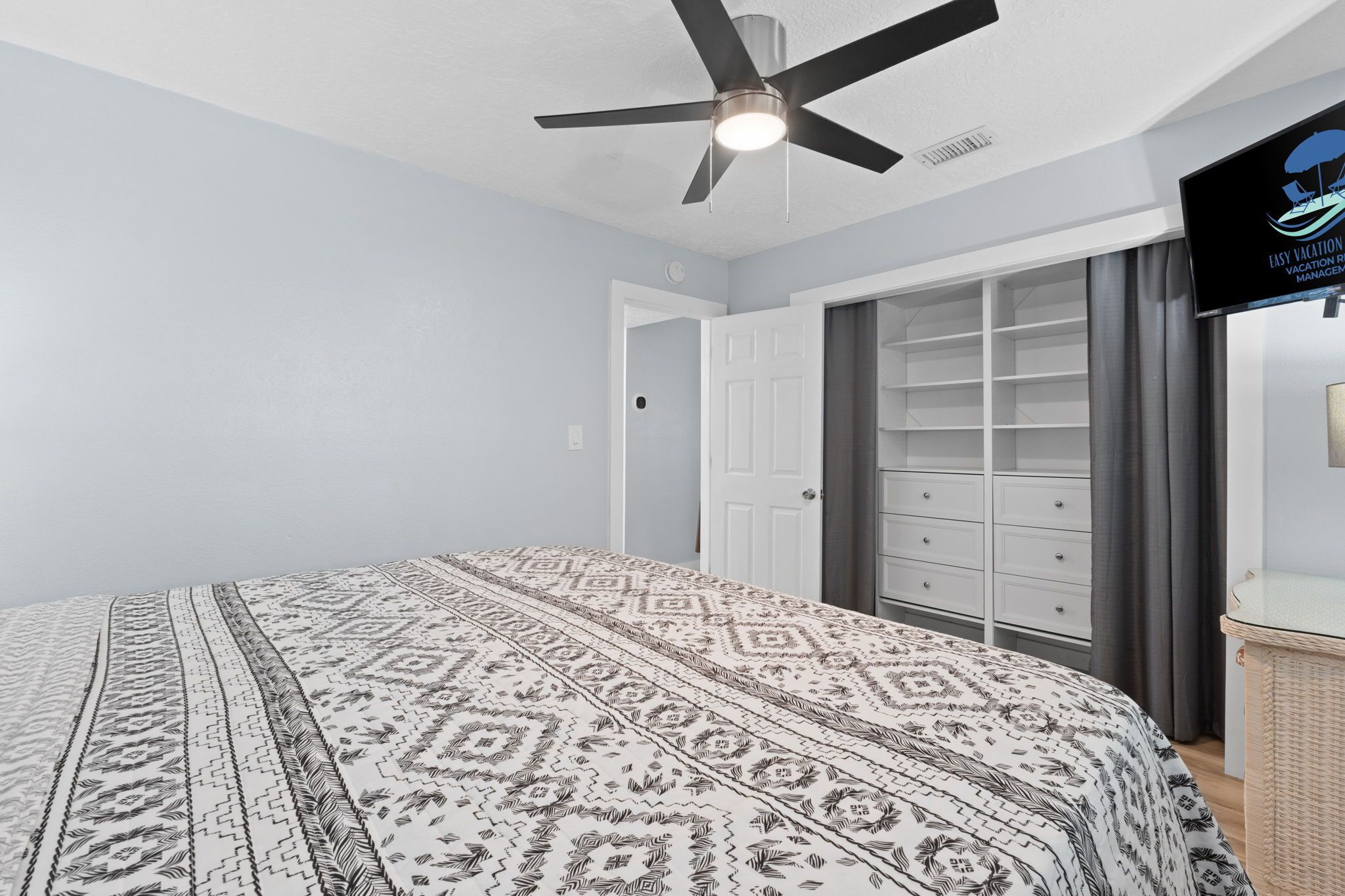 A bedroom with a bed, a ceiling fan, a wardrobe, and a television.