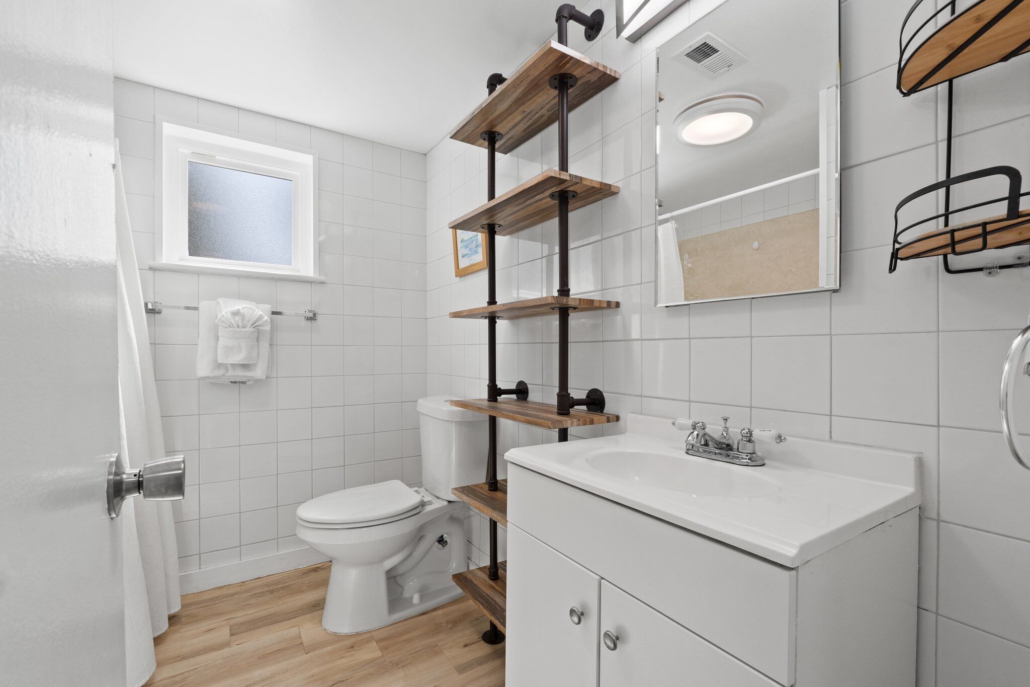 Une salle de bain avec des toilettes blanches, un lavabo et des étagères en bois.