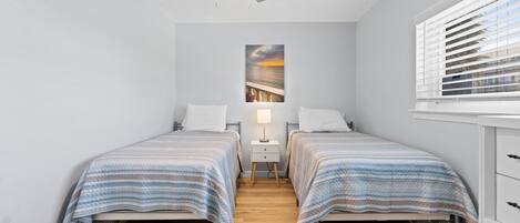 A bedroom with two single beds, a ceiling fan, a nightstand with a lamp, and a window with blinds.