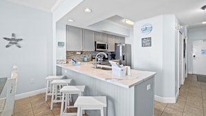 Een moderne keuken met grijze kastjes, een marmeren eiland en barstoelen.