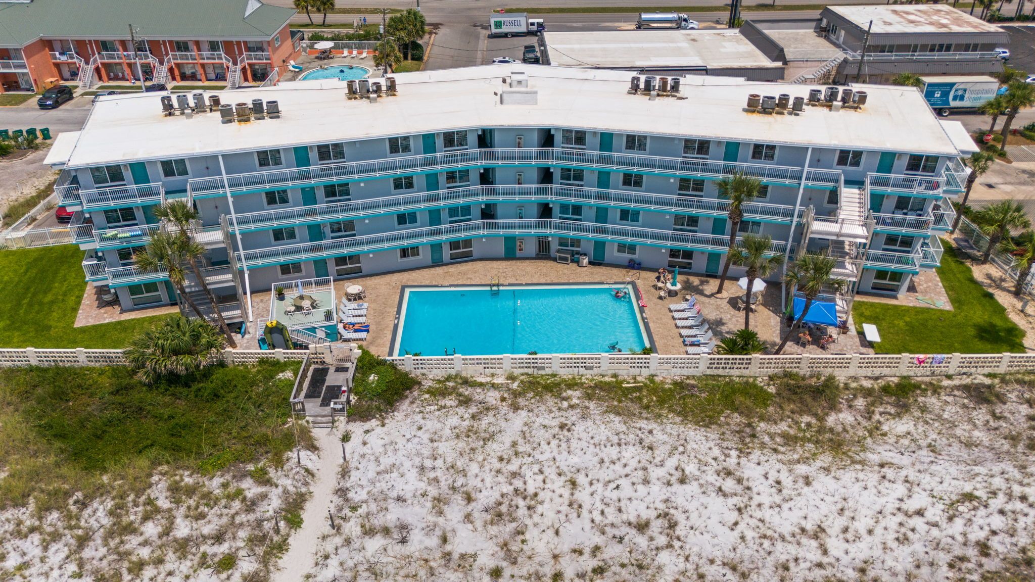 A multi-story hotel with a central pool, outdoor seating, and a beach view.