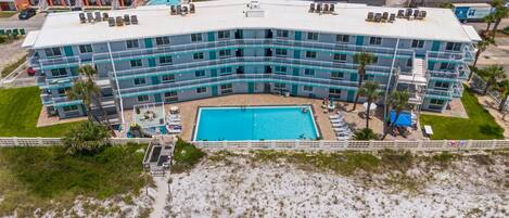 A multi-story hotel with a central pool, outdoor seating, and a beach view.
