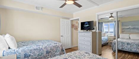 A bedroom with two beds, a ceiling fan, a television, and a door leading to another room.