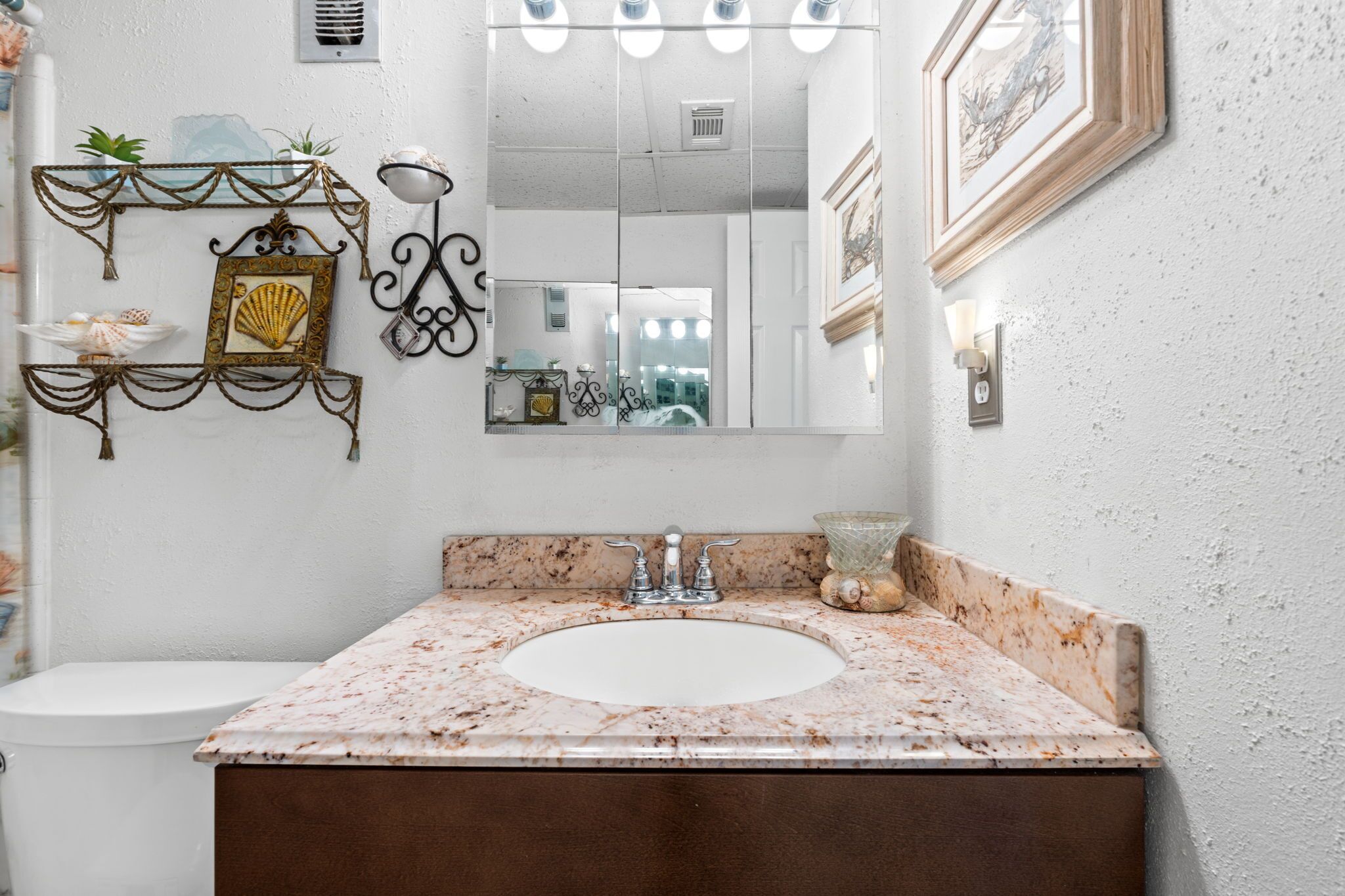 A bathroom with a marble sink, a large mirror, and decorative wall sconces.