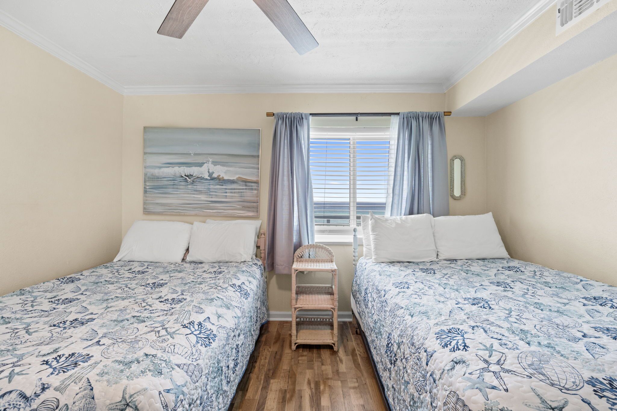 Quarto com duas camas, um ventilador de teto, uma janela com cortinas e um quadro na parede.