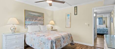 A bedroom with a bed, two nightstands, a ceiling fan, and a door leading to another room.