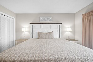 Une chambre à coucher avec un grand lit, deux tables de chevet avec des lampes, une tête de lit et un élément décoratif mural.