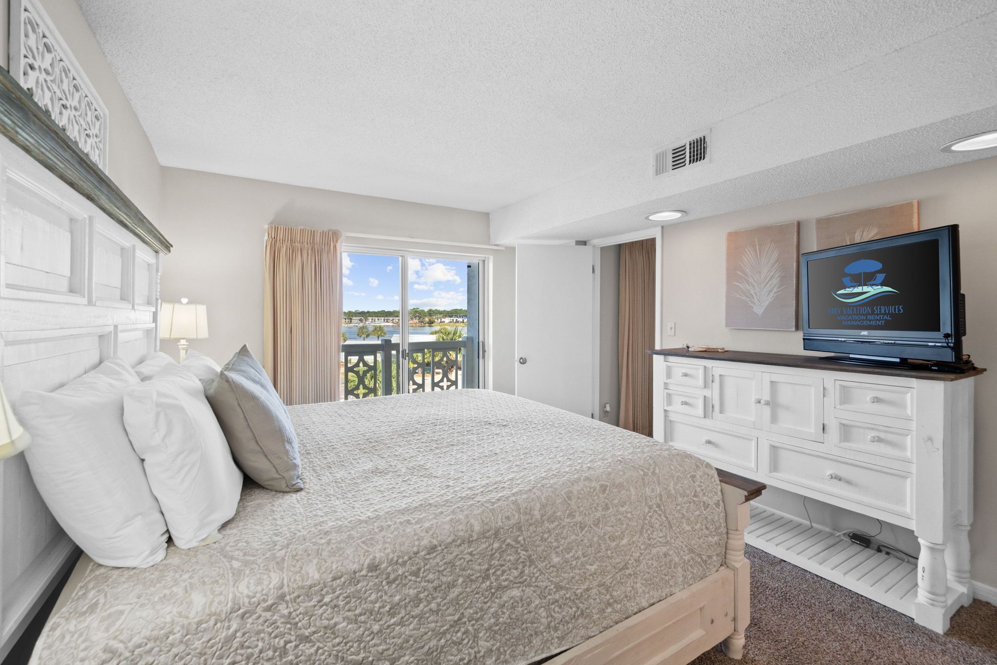 A bedroom with a bed, a TV, a dresser, and a balcony with a view.
