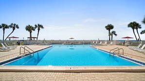 Ein rechteckiger Swimmingpool mit klarem, blauem Wasser, umgeben von Liegestühlen und Palmen.