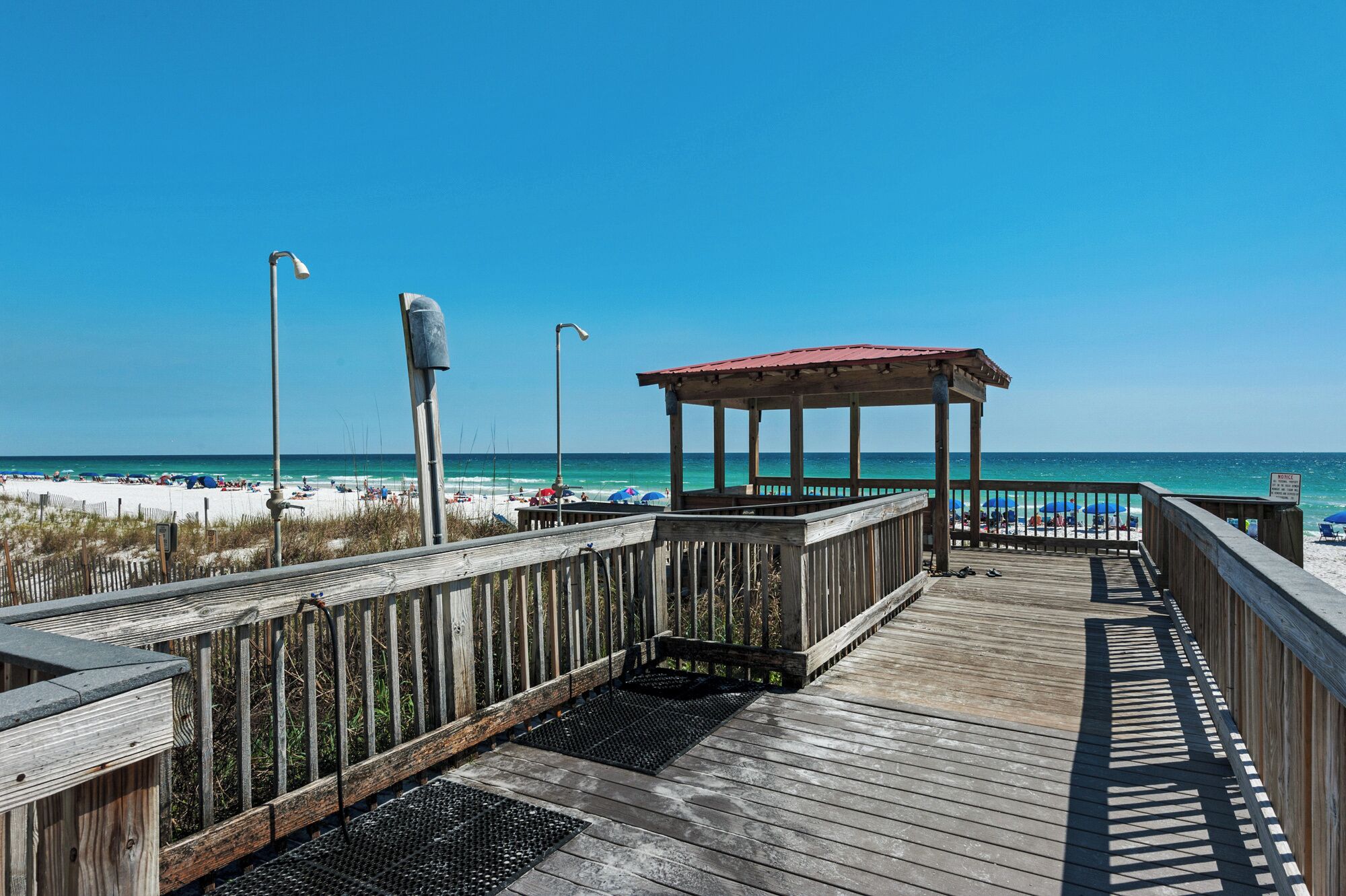 A wooden boardwalk leading to a beach with a gazebo and umbrellas.
