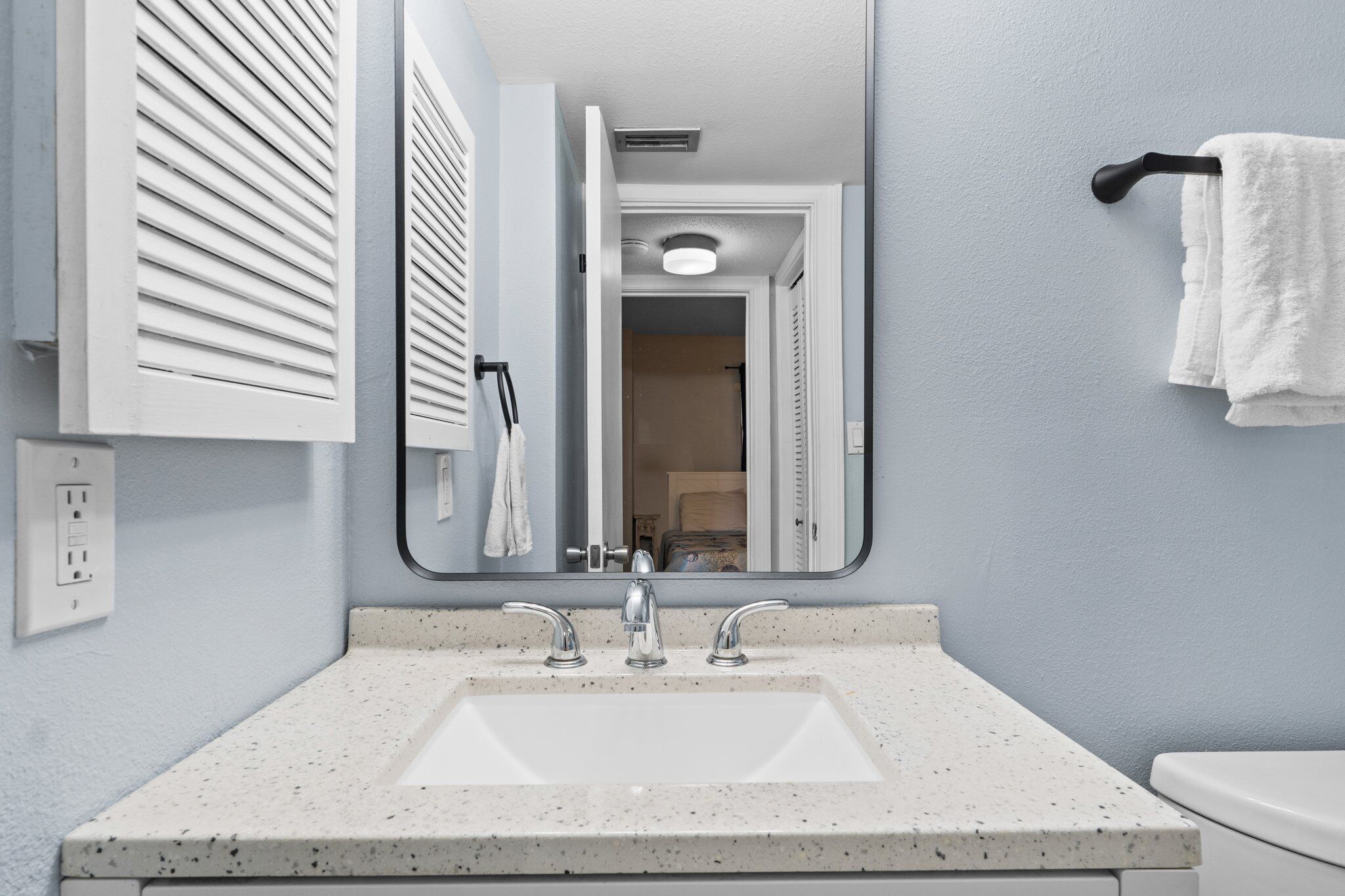 Un bagno con un lavandino bianco, due rubinetti, uno specchio e un portascopevoli.