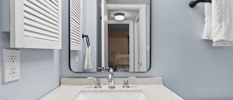 Un bagno con un lavandino bianco, due rubinetti, uno specchio e un portascopevoli.