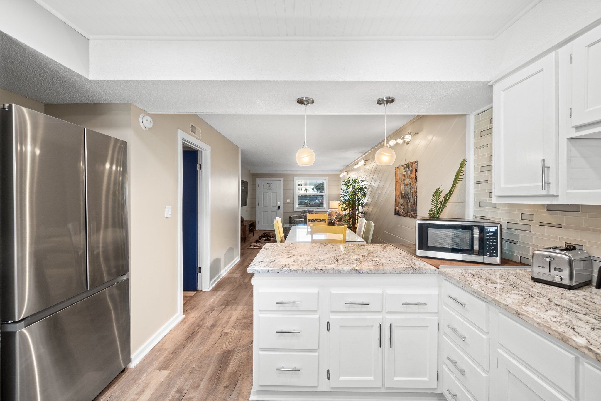 A modern kitchen with white cabinetry, a stainless steel refrigerator, a microwave, and a toaster.