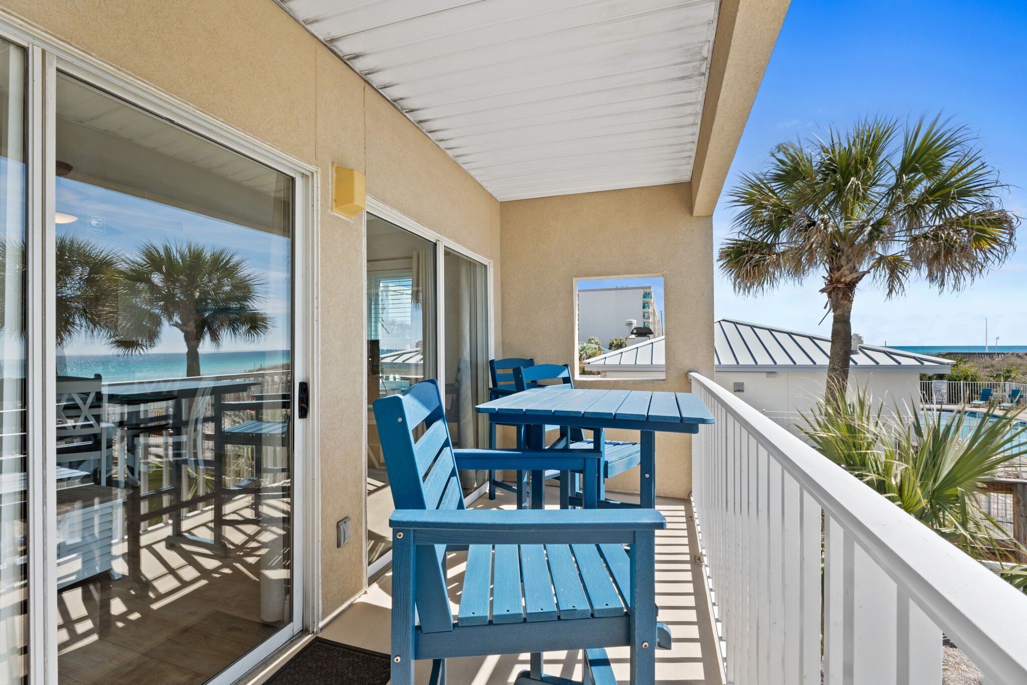 Ein Balkon mit blauen Stühlen und Tischen, einer Palme und Blick auf das Meer.