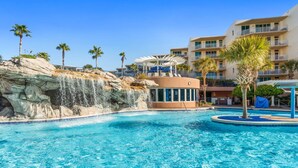 Una piscina con una cascada, palmeras y un edificio con balcones.