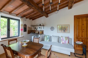 A cozy room with a wooden dining table, a white sofa, and a kitchen area with a shelf above.