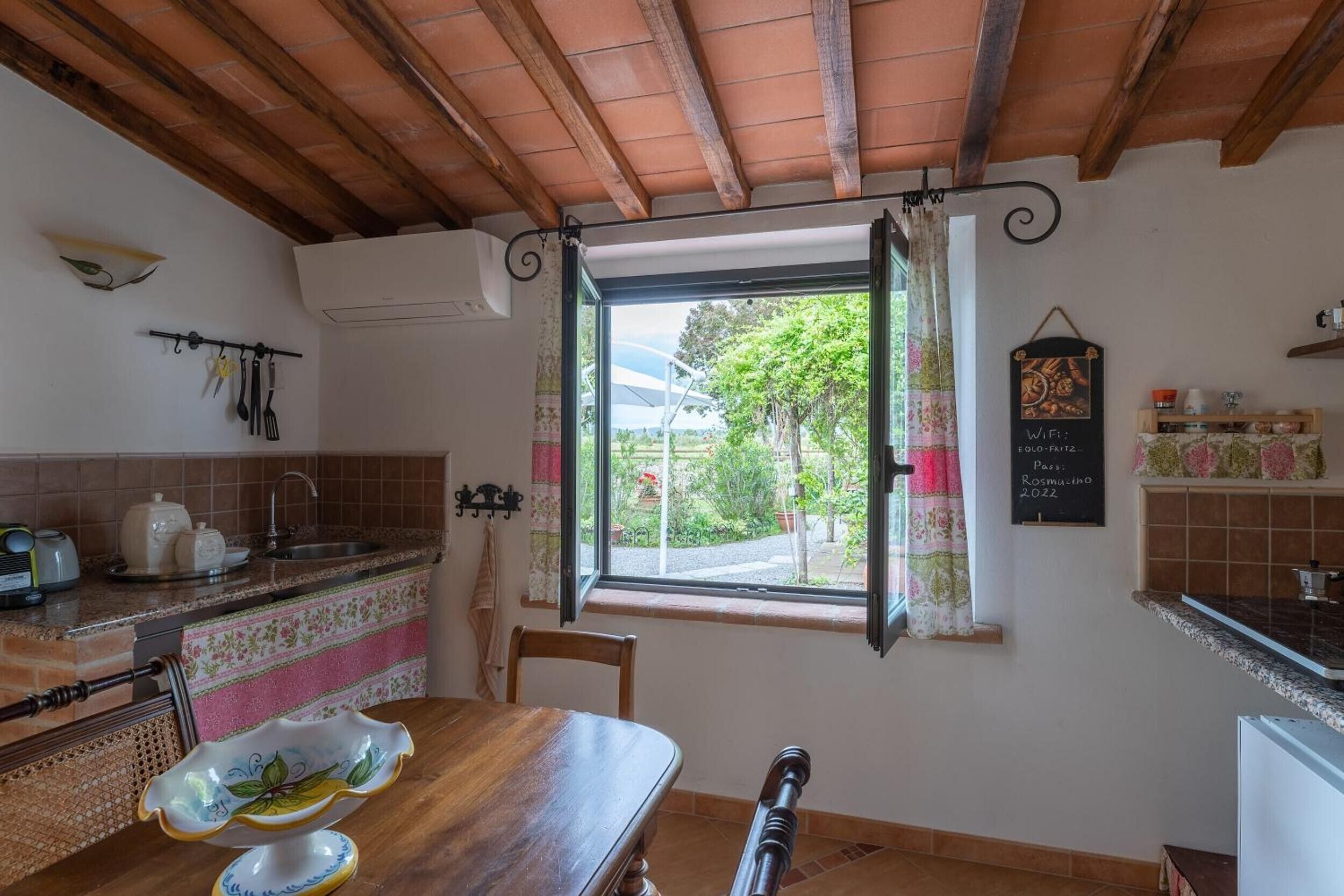 A kitchen with a wooden table, a window with curtains, a hanging light fixture, and a chalkboard sign.