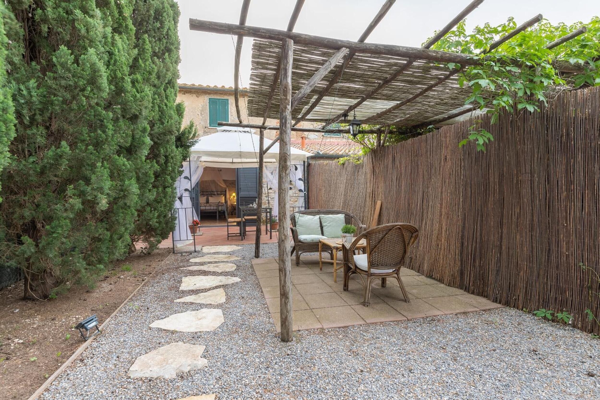 Un espace patio agrémenté d’une pergola, de sièges d’extérieur et d’un chemin de pierre menant à un bâtiment.