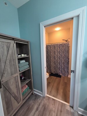 Une salle de bain avec une douche, des toilettes et un meuble en bois doté d’étagères.