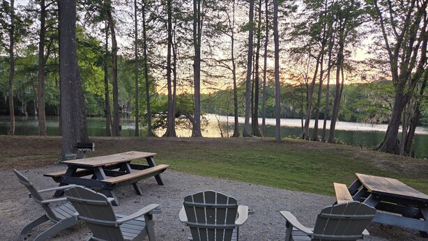 A picnic area with tables and chairs, surrounded by trees and a lake.