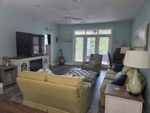 Ein Wohnzimmer mit Fernseher, Gitarre, einem gemusterten Sessel und einer Couch.