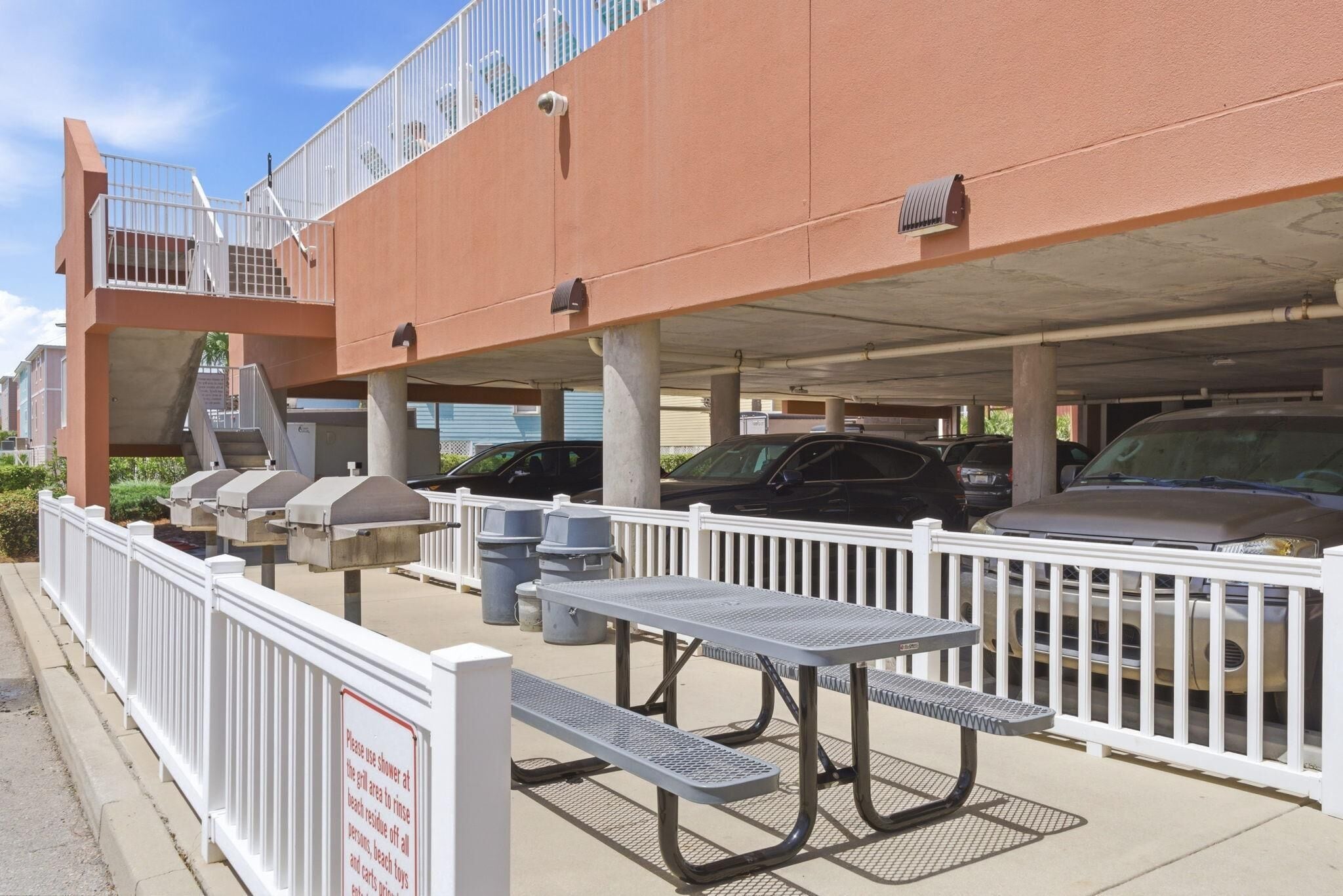 A parking garage with a covered walkway, picnic tables, and a white fence.