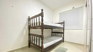 Uma cama beliche num quarto com paredes brancas e uma janela com persianas.