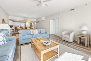 A modern living room with a blue sofa, wooden coffee table, and a white armchair. - Ocean View 138th Street 3 BR, sleeps 12 with pool (Ocean City)