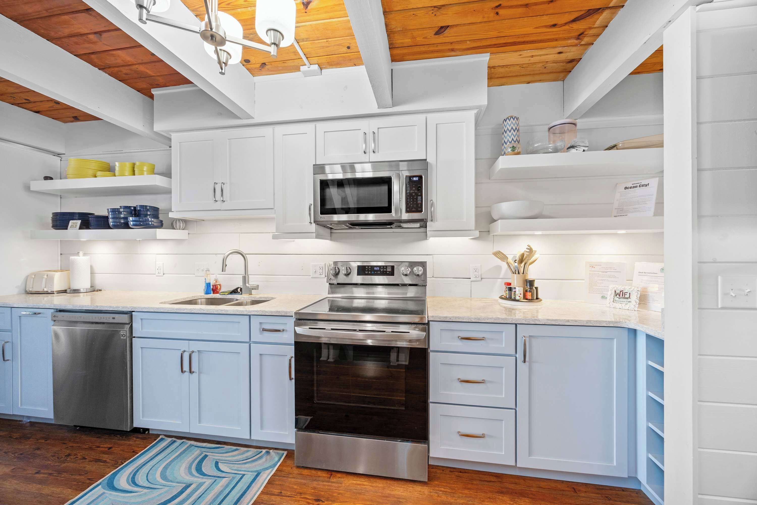 A modern kitchen with white cabinets, stainless steel appliances, and a wooden ceiling.