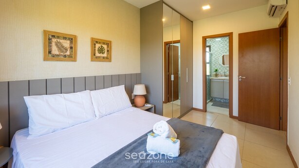 A hotel room with a bed, a bedside table with a lamp, and a towel on the bed. - Apt in Condo w/ Pool 750 m Beach Rdw0103 (Camaçari)
