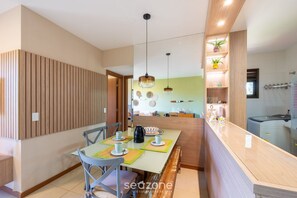 A modern kitchen with wooden cabinetry, a dining area with a table and chairs, and pendant lighting. - Apt in Condo w/ Pool 750 m Beach Rdw0103 (Camaçari)
