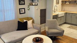 A modern living room with a sofa, armchair, and coffee table. There is a kitchen area with shelves and a sink. - Cozy East Nashville Home w Fenced-In Backyard (Nashville)