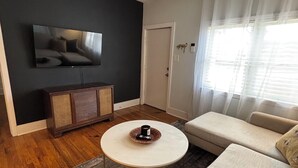A modern living room with a flat-screen TV, a round coffee table, a sofa, and a dark accent wall. - Cozy East Nashville Home w Fenced-In Backyard (Nashville)