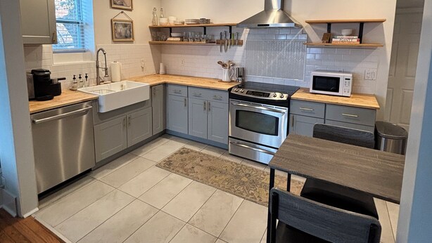 A modern kitchen with stainless steel appliances, wooden countertops, and a herringbone tile backsplash. - Cozy East Nashville Home w Fenced-In Backyard (Nashville)