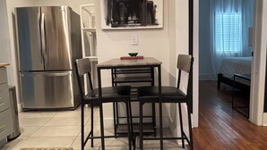 A compact kitchen with a stainless steel refrigerator, a dining table with four chairs, and a modern abstract painting above the table. - Cozy East Nashville Home w Fenced-In Backyard (Nashville)